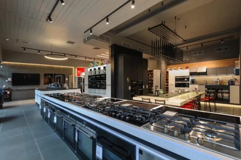 Modern kitchen appliance showroom featuring rows of stoves, ovens, and various kitchen equipment on display under ceiling lights.