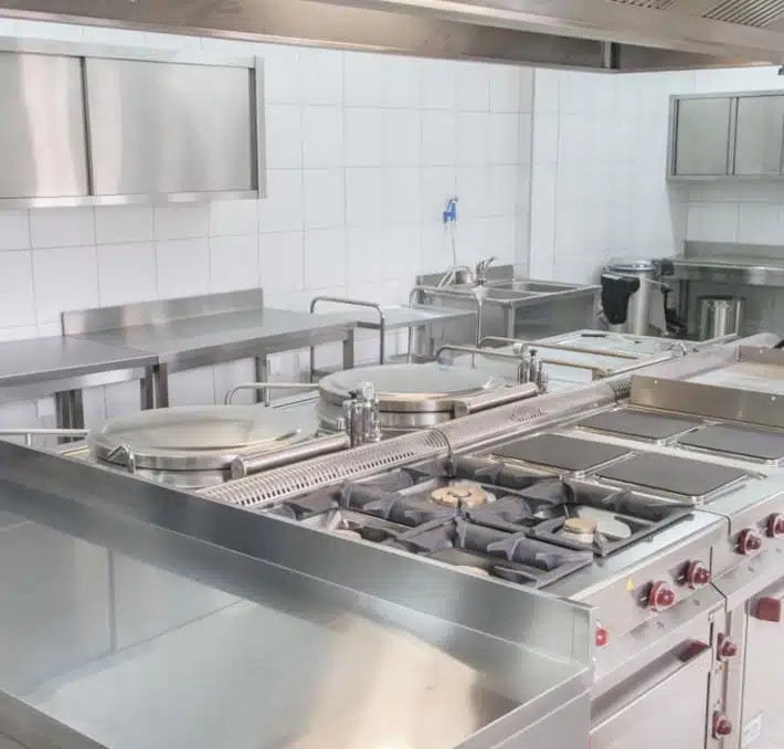 A commercial kitchen with stainless steel appliances, gas stoves, countertops, sinks, and tiled walls.