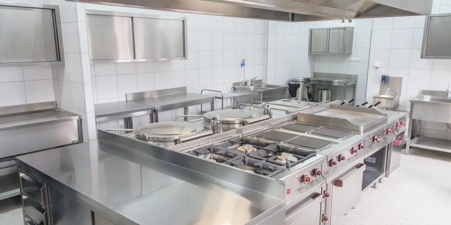 A commercial kitchen with stainless steel appliances, countertops, stoves, sinks, and storage cabinets, all in a clean, organized environment.