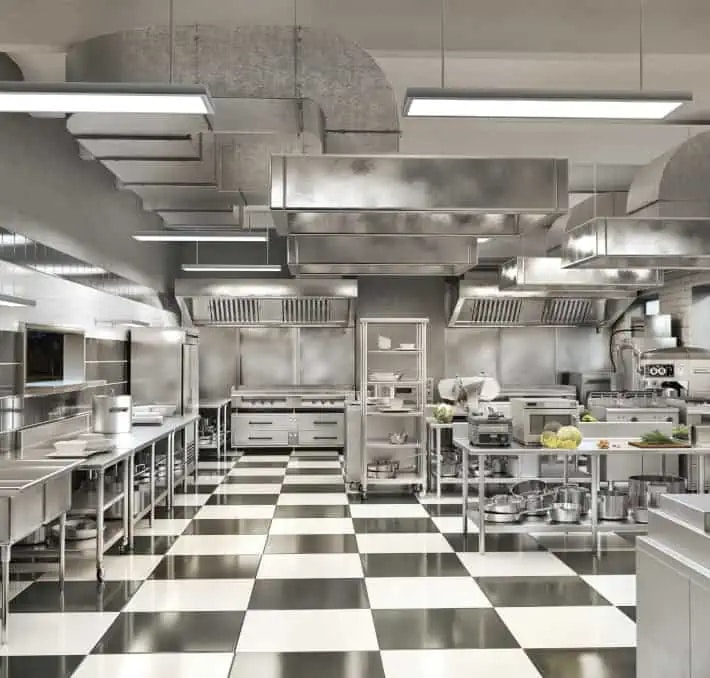 Commercial kitchen with stainless steel appliances, counters, and ventilation hoods, featuring a black and white checkered floor and overhead fluorescent lighting.